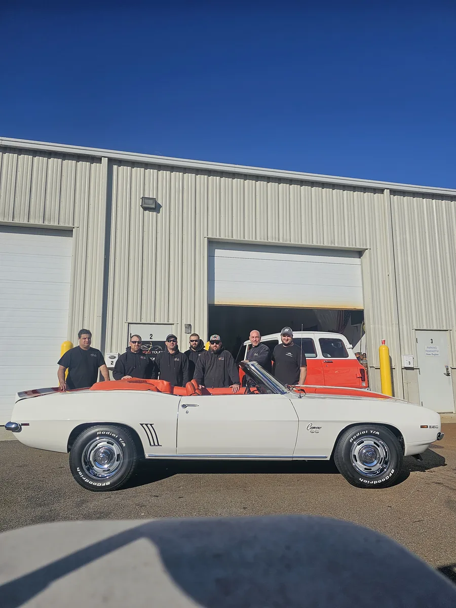 The Angels Touch team standing behind a white Camaro convertible outside the shop