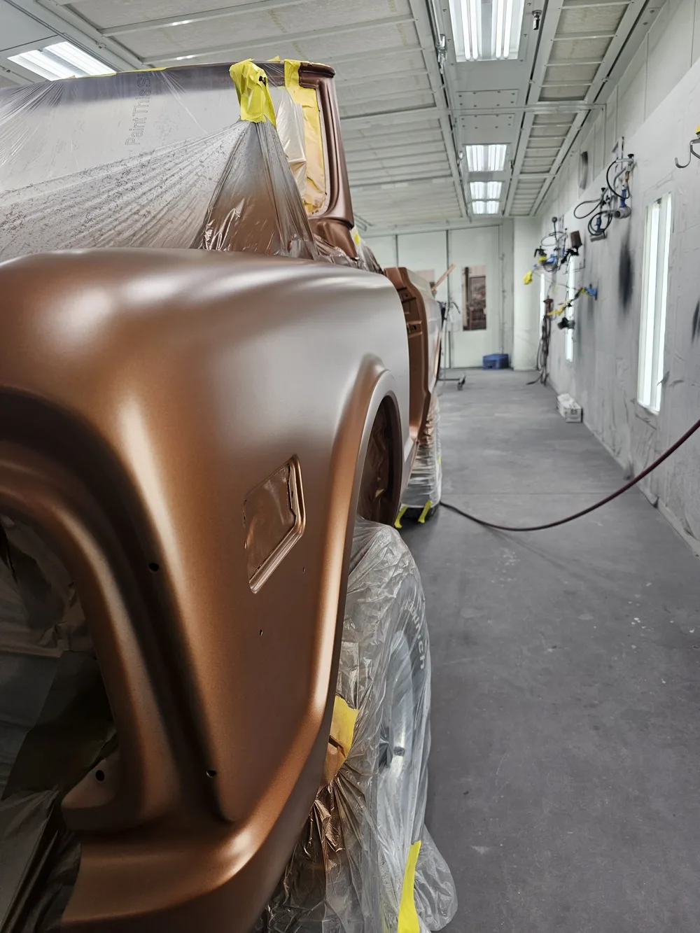 Bronze truck fender being prepped and painted inside a spray booth